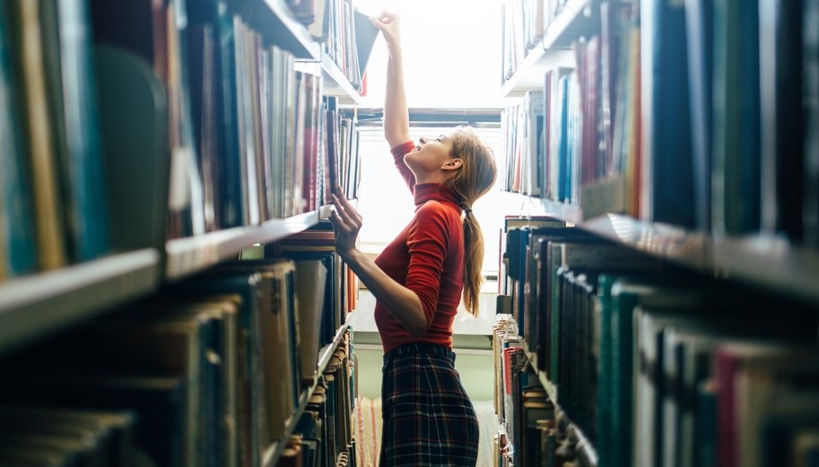 Mujer alcanzando un libro en una estantería de biblioteca